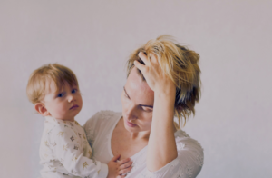 Młoda, zmęczona mama trzymająca płaczące niemowlę – wsparcie psychologiczne w okresie matrescencji.